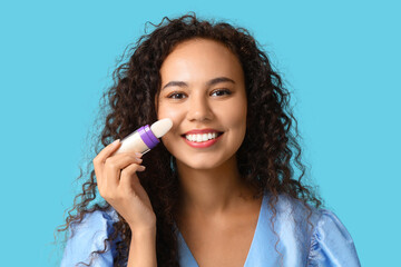 Wall Mural - Beautiful young happy African-American woman with foundation on blue background