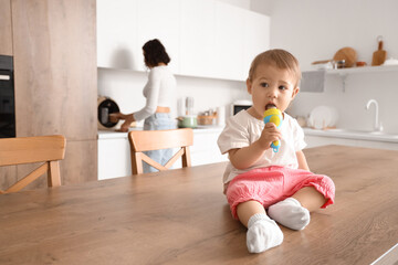 Poster - Cute little baby with nibbler eating food on table in kitchen