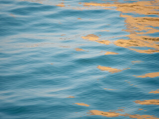 Wall Mural - Beautiful close up sea water surface, blue water with golden sunrise reflections. Close-up of golden water with calm ripples surface.