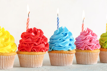 Wall Mural - Different sweet Birthday cupcakes with burning candles on light blue table