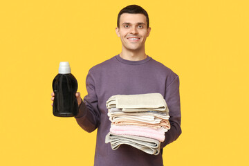 Canvas Print - Young man with clean towels and bottle of detergent on yellow background