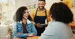 © PeakPoints/peopleimages.com - Coffee shop, women and waiter with tablet, conversation and customer service order at restaurant. Barista, staff and happy girl friends with smile and chat at diner with employee helping with tech