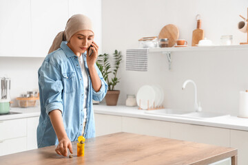 Wall Mural - Young woman after chemotherapy with weed talking by mobile phone in kitchen