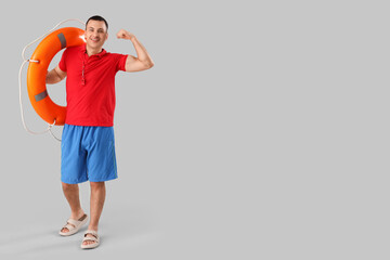 Wall Mural - Happy male lifeguard with ring buoy showing muscles on grey background