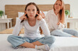 © Pixel-Shot - Teenage girl covering her ears while her mother arguing in bedroom. Family difficulties concept