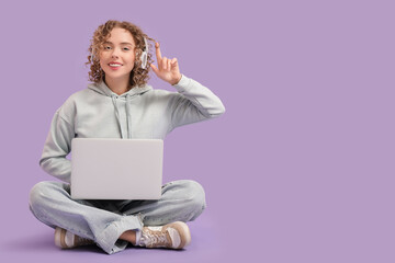 Canvas Print - Thoughtful young woman in headphones with laptop sitting on lilac background