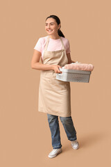 Poster - Beautiful young happy woman with basket of clean towels on beige background