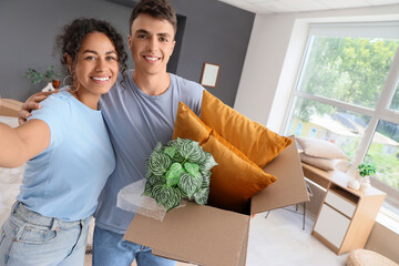 Wall Mural - Young couple with box taking selfie in room on moving day