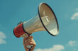 © Rattanapon - Hand holds white and red megaphone against the blue sky.