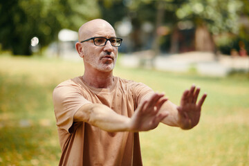 senior african american man standing in sunny park stretch hands in front, enjoying peaceful outdoor