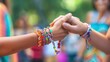 © NewMaii - Close-up of two hands clasping together, adorned with colorful bracelets, symbolizing friendship and connection.