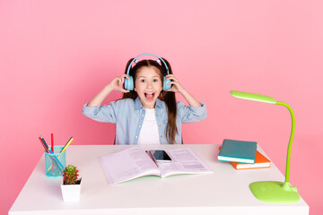 Wall Mural - Photo of overjoyed girl dressed shirt sit down table in headphones listen music on smartphone have fun isolated on pink color background