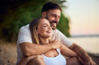 © bnenin - Happy couple laughing together while sitting by the lake, spending time together.