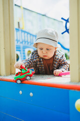 Wall Mural - A little boy plays with toys on the street during a walk. A boy in panama on his head and a shirt on a sunny day. clothes for babies