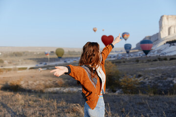 Wall Mural - Woman with arms outstretched in front of colorful hot air balloons floating in the sky