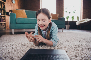 Poster - Portrait of cute little girl lying floor talk video call lesson laptop loft interior modern flat indoors