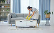 © peopleimages.com - Cleaning, tidy and woman by table in living room for organising, remove dirt or doing chores. Magazine, gloves and domestic worker with apron for housekeeping, maid service or maintenance in home