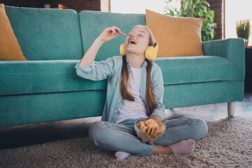 Wall Mural - Full length portrait of cute little girl listen music eat cookies wear shirt loft interior modern flat indoors