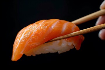 Chef hand holding a piece of salmon sushi with chopsticks against a black background