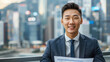 © ChubbyCat - Pension Consultant,  An optimistic Asian male in his 30s showing a financial report on retirement plans in a suit and tie on a sleek urban skyline background.