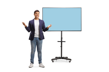 Poster - Full length portrait of a happy young man in jeans and suit presenting in front of tv screen on a stand