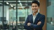© Thanos - Confident Asian Businessman Smiling with Arms Crossed in Office Setting
