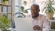 © Natpasit - A focused professional in a white shirt works on a laptop at a home office, surrounded by plants and natural light..