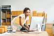 © Phushutter - An African American woman with an afro works at a wooden desk, equipped with a laptop, desktop computer, and parcel cardboard boxes, focusing on SME logistics, inventory, and online orders.