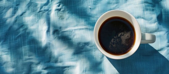 Wall Mural - Morning scene with a white cup of black coffee set against a blue textile background ideal for a copy space image