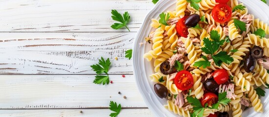 Aufkleber - Top view of a fusilli pasta salad with tuna tomatoes olives and parsley on a white wooden backdrop featuring copy space for images