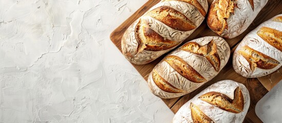 Poster - A high quality photo of a bakery display featuring golden rustic loaves of bread on a wooden board placed on a light background captured from above with a layout including copy space image