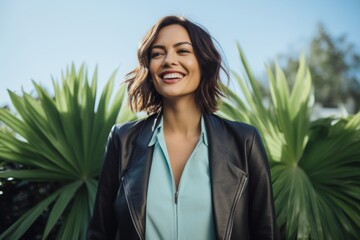 Wall Mural - Portrait of a blissful woman in her 30s sporting a stylish leather blazer in pastel blue background