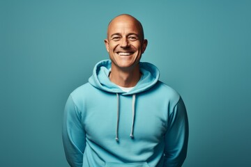 Wall Mural - Portrait of a grinning man in his 40s wearing a zip-up fleece hoodie in pastel blue background