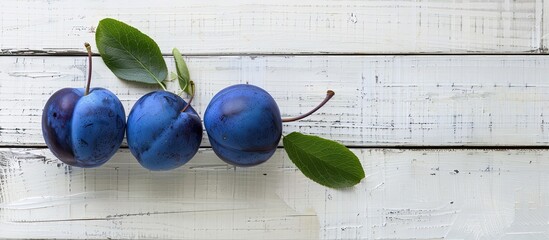 Poster - Three blue plums and a green leaf on a white wooden surface with ample copy space image