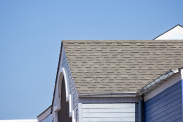 A roof with a blue house in the background. roof shingle and blue sky background.