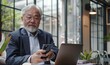 © Raool - Senior middle aged Asian businessman manager ceo using smartphone and laptop in office working online, Generative AI