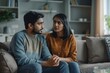 © Raool - Indian woman calming upset offended guy, support and caring, sitting on sofa at home, free space. Sorry after quarrel, relationship problems, bad news, Generative AI