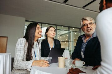 Wall Mural - coworkers chatting at a conference table, discussing ideas and networking in a modern office environ