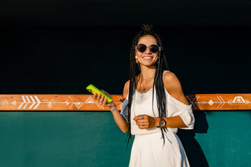 Wall Mural - beautiful tanned smiling skinny woman posing on summer tropical vacation in white trendy dress using smartphone