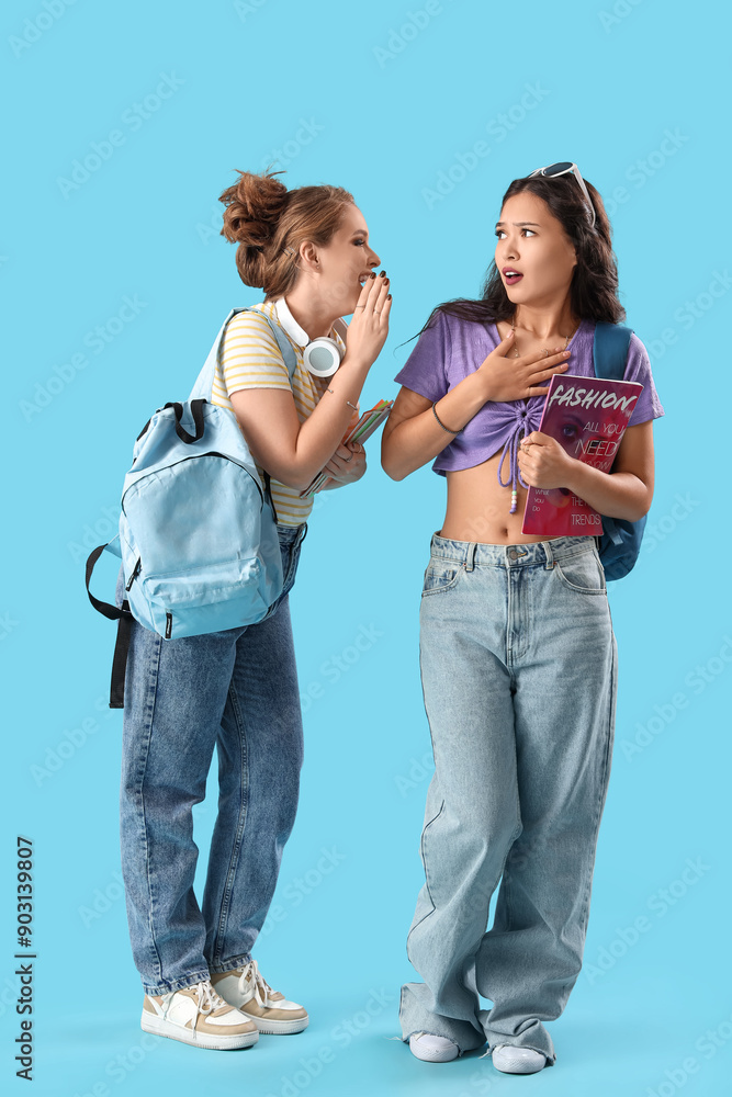 Female students gossiping on blue background