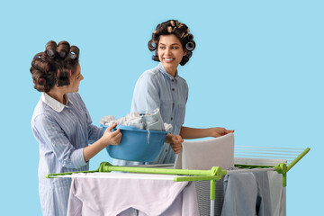 Poster - Little girl and her mother with hair curlers hanging laundry on dryer against blue background