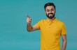© Cetin - Young happy man in yellow polo pointing finger up to side on light blue background