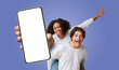 © Prostock-studio - A young multiracial couple is holding a smartphone with a blank screen in front of them. The woman is giving a thumbs up while riding on the man's back.