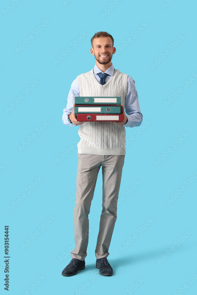 Young businessman with stack of folders on blue background