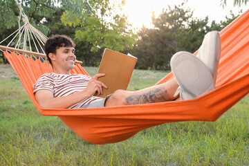 Wall Mural - Young man with book resting in hammock outdoors