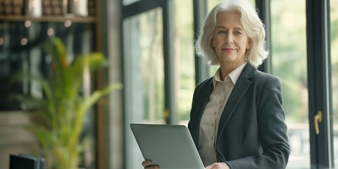 Wall Mural - A woman in a business suit holding a laptop. She is smiling and she is happy. Concept of professionalism and confidence