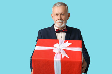 Sticker - Handsome mature man in stylish formal suit with bow tie and gift box on blue background