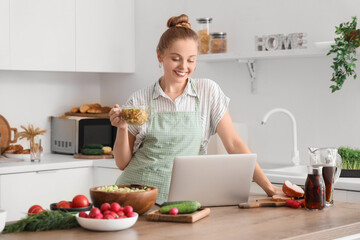 Canvas Print - Young woman with tasty okroshka and laptop in kitchen