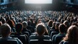 © svastix - This image captures the back view of a large audience seated in a theater hall, attentively watching something on a screen in front of them. The hall is packed.