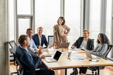 Aufkleber - A group of diverse business professionals, including a woman standing, are gathered around a conference table in a modern office. They are working together on a project, engaging in discussion